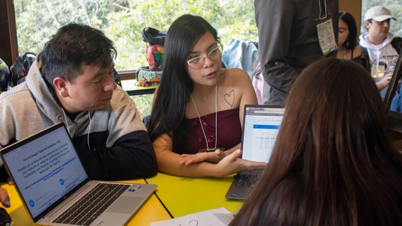 Estudiantes jóvenes sostienen una conversación alrededor de un computador.